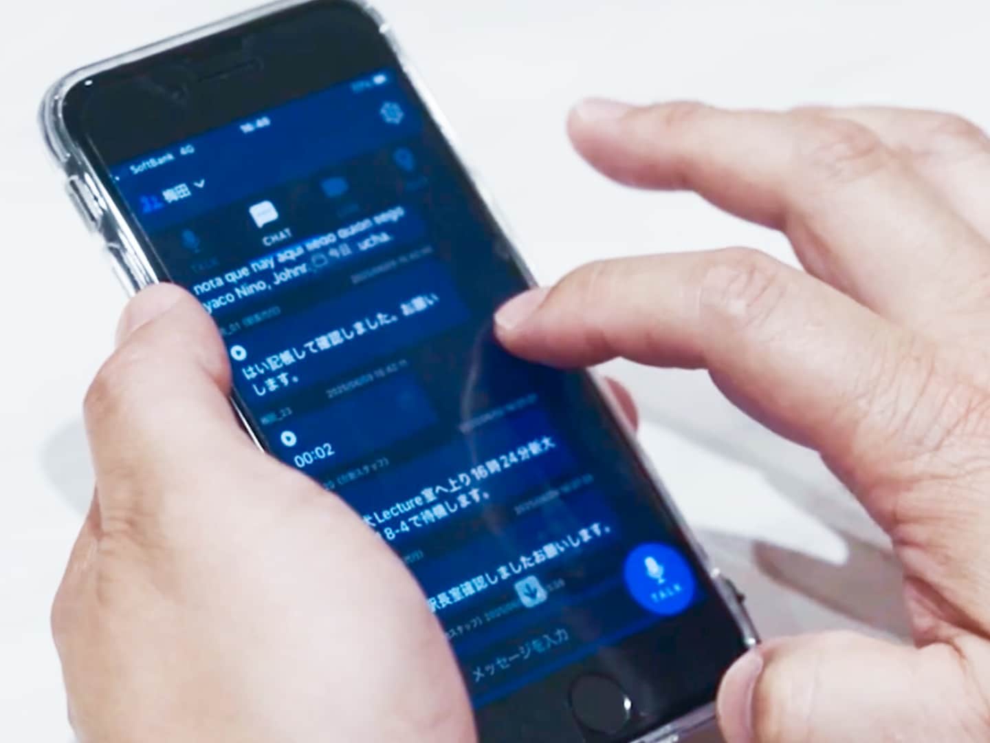 手に持たれたスマートフォンの画面には、チャットメッセージが表示されている。