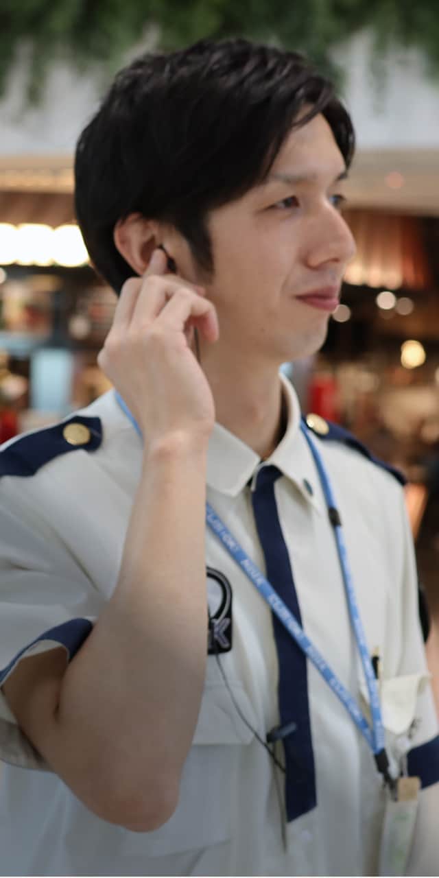 商業施設内で、制服を着た男性がイヤフォンをつけて耳に手を当てている様子。