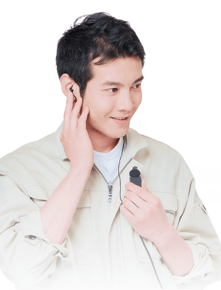 白い服を着た男性がイヤフォンを装着し、マイクを持ちながら微笑んでいる。